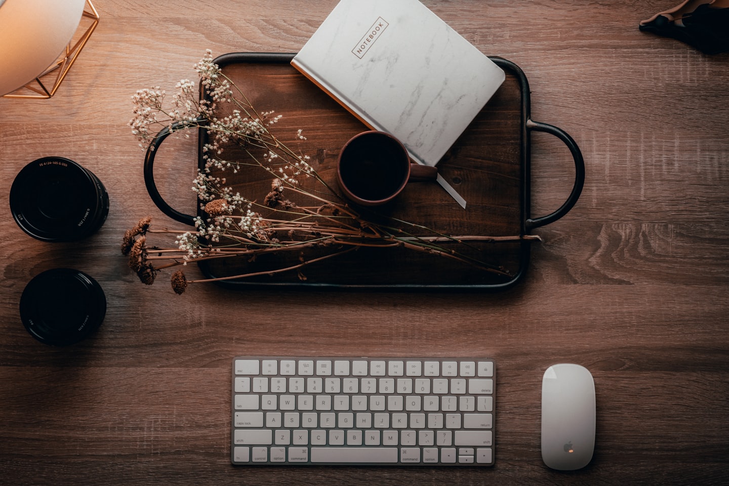 Organized wooden desk with notebook, mug, and camera lenses.