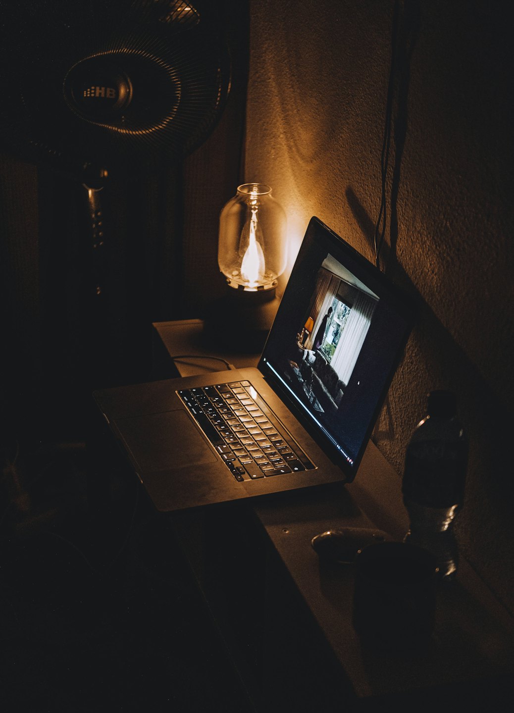Laptop with video on desk near lamp and water bottle.